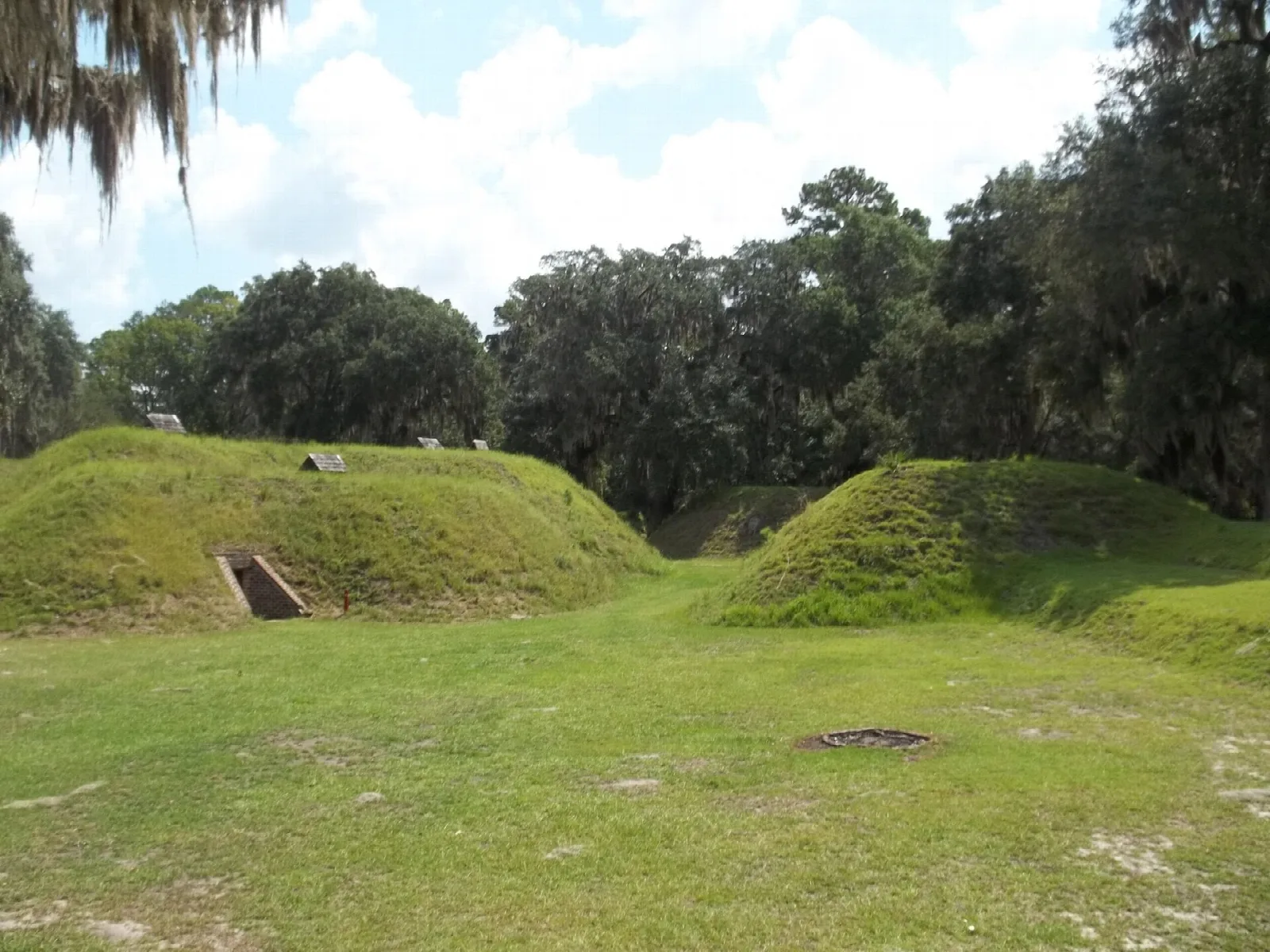 Grass-covered earthwork mounds under live oaks