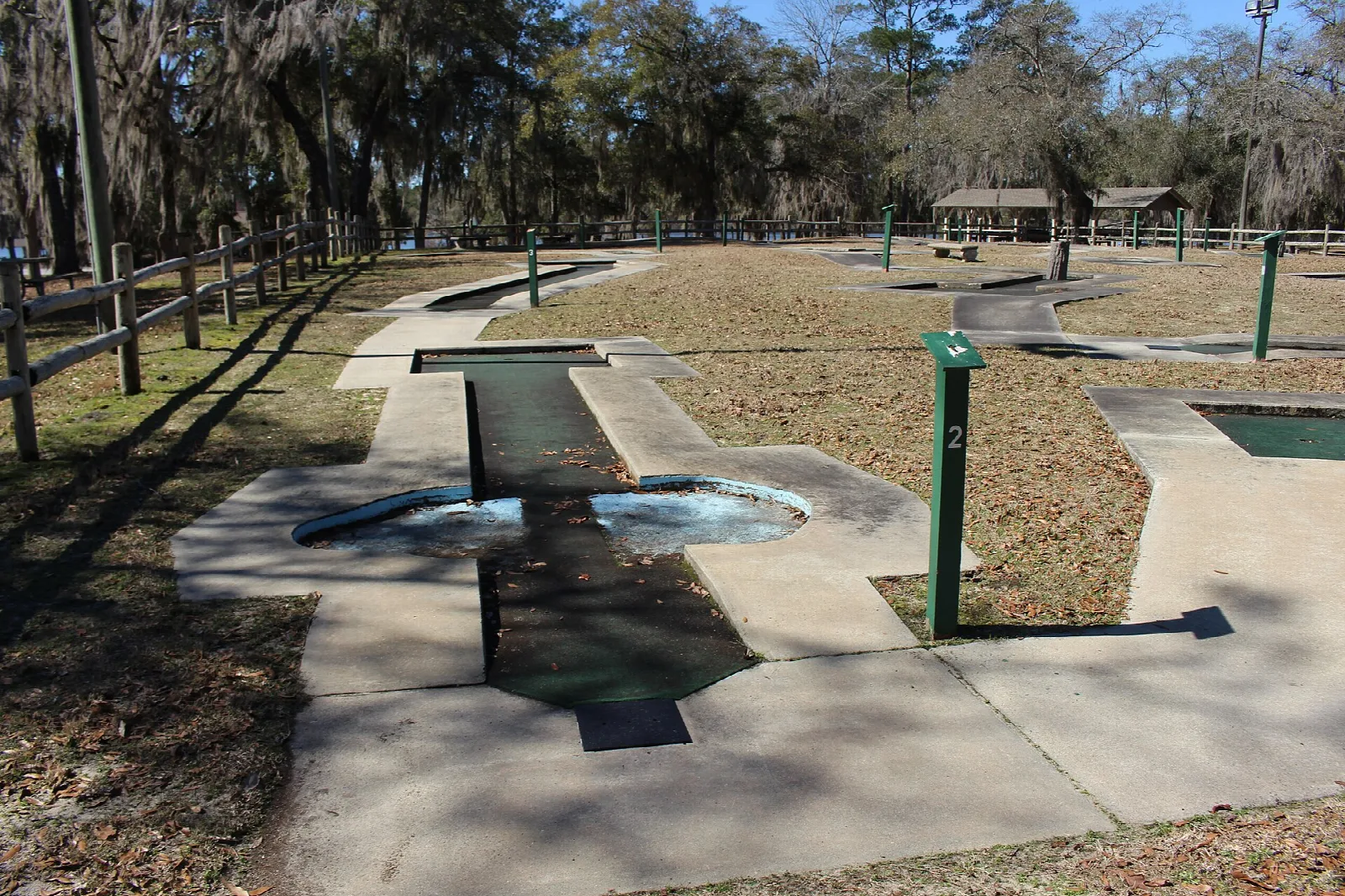 Miniature golf hole with a small water hazard among oak trees