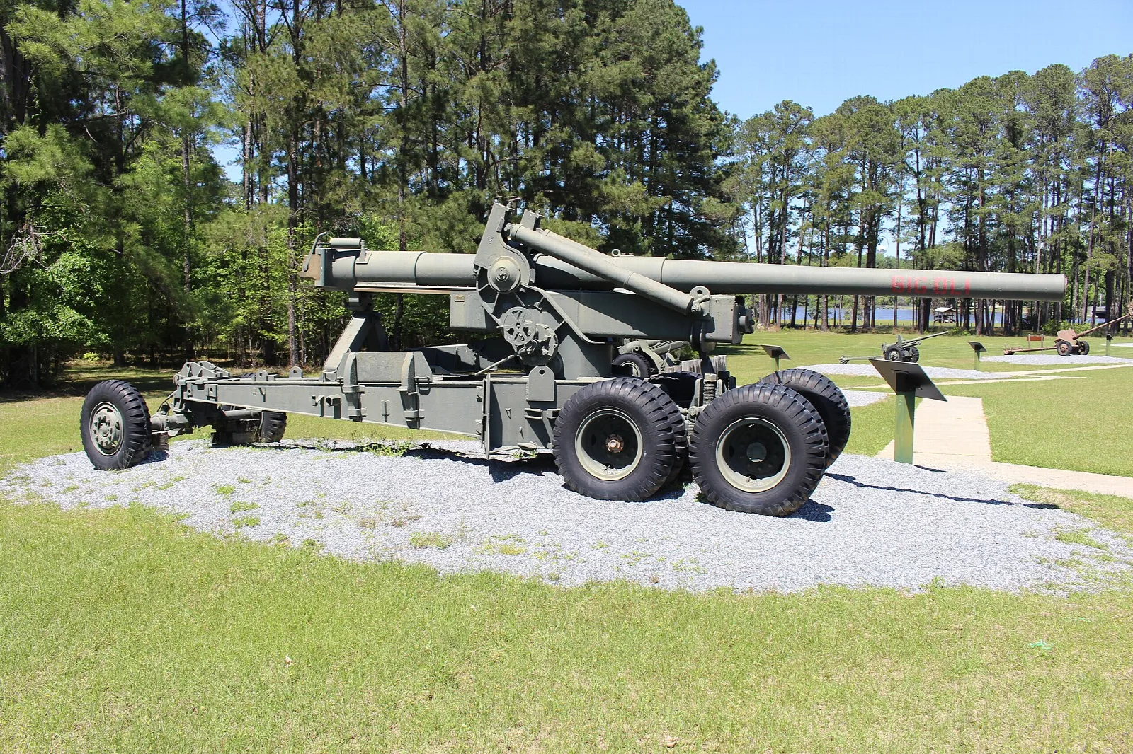 Large green field gun on a gravel pad with tall pines behind
