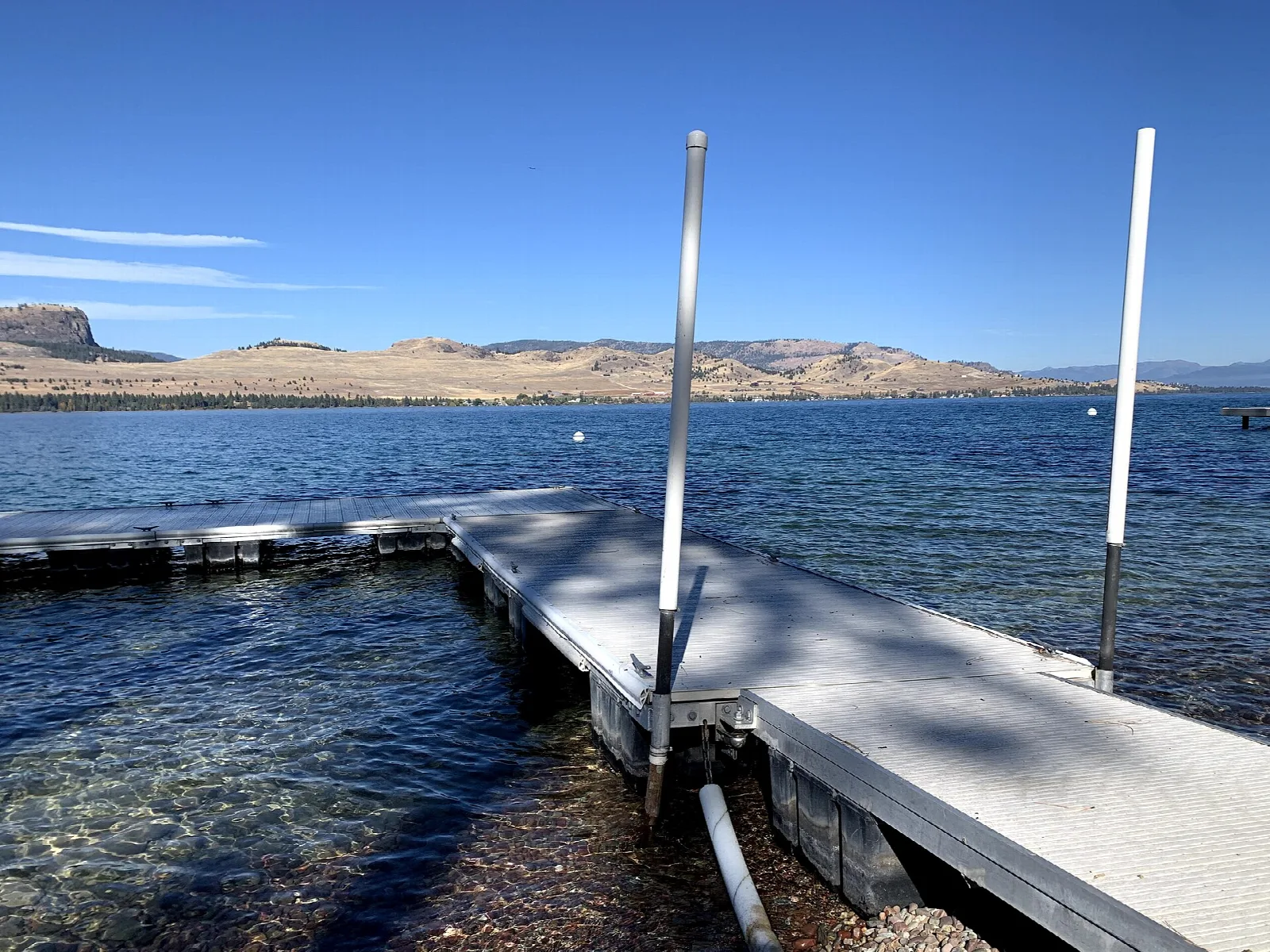 Gray floating dock extending into clear blue lake water, with tan hills beyond