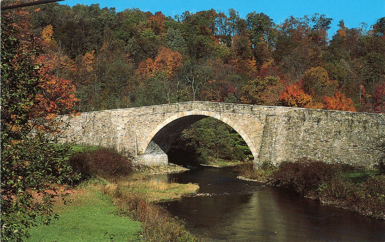 Stone arch bridge over a river surrounded by autumn trees