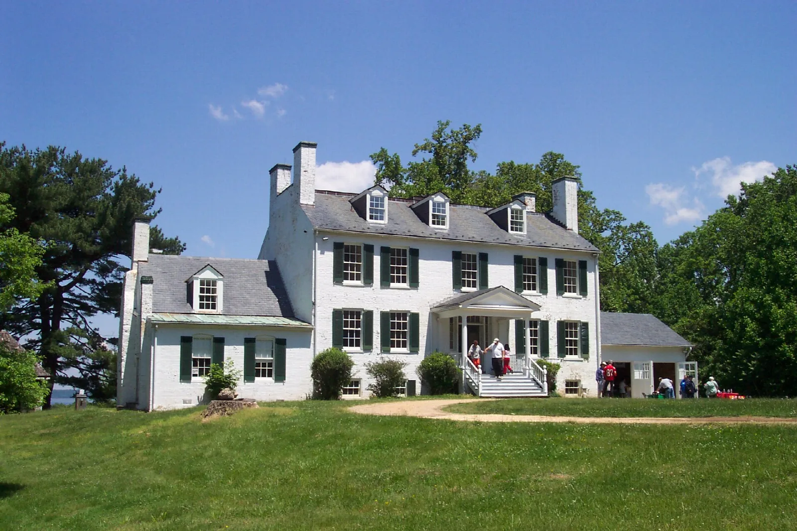 White two-story manor house with dark shutters on a green lawn