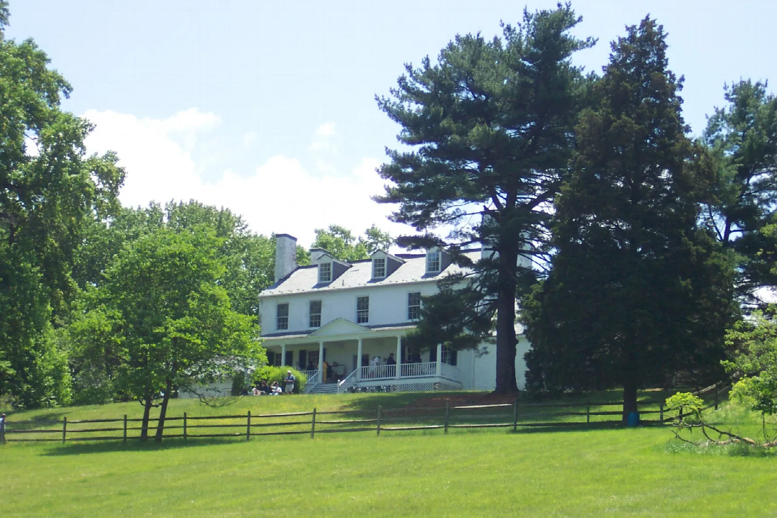 Wide view of a white manor house across a lawn with tall pines