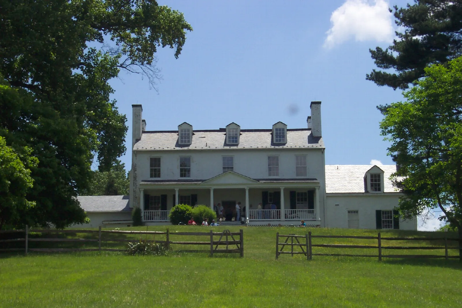 White manor house with dormers behind a wooden fence and lawn