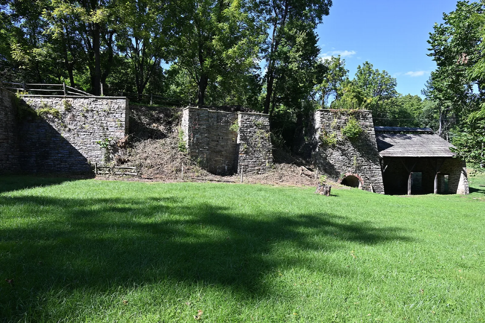 Old stone furnace walls and a wooden shed on a green lawn