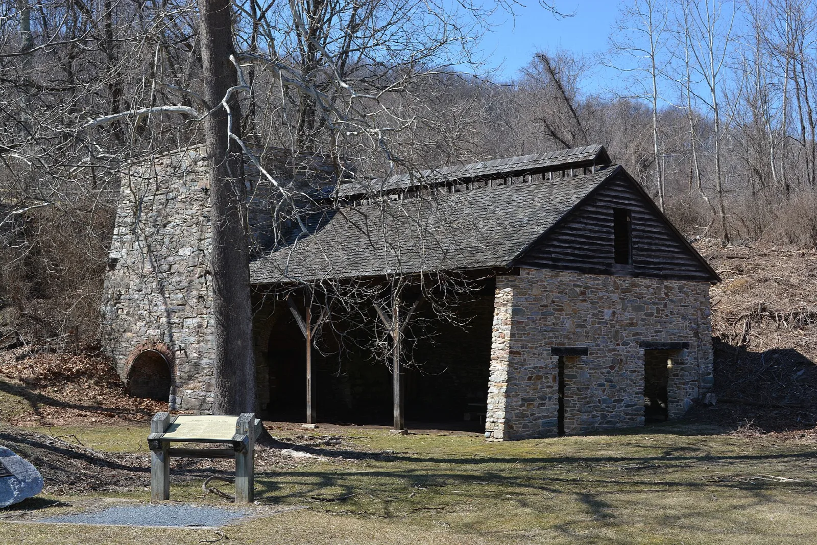 Stone furnace with a dark wooden roofed shed among bare trees