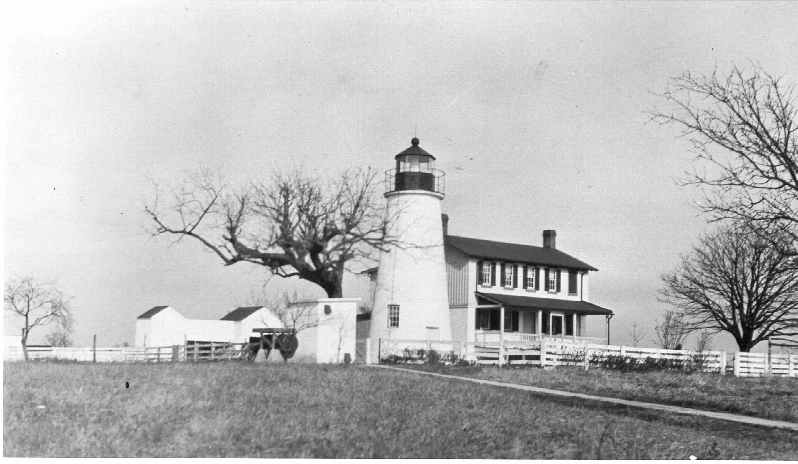 Black and white photo of a lighthouse and keeper's house in an open field
