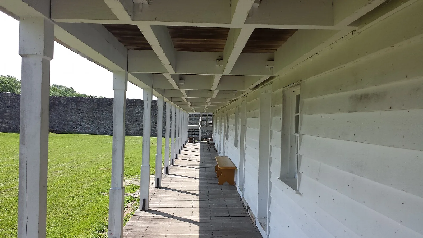 Covered wooden walkway along a white barracks building beside a lawn