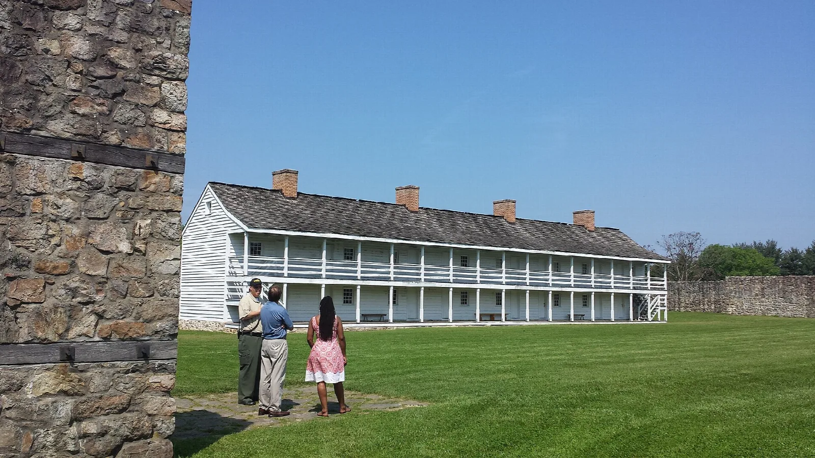 Two-story white barracks with a long porch across a green lawn