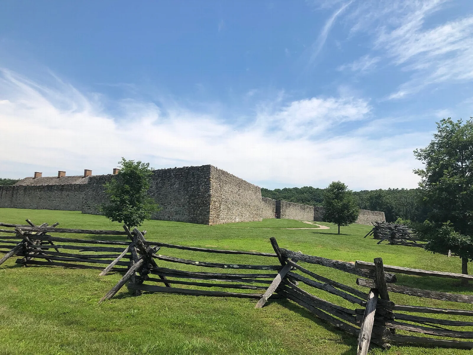Stone fort walls beyond a split-rail fence and green grass under blue sky