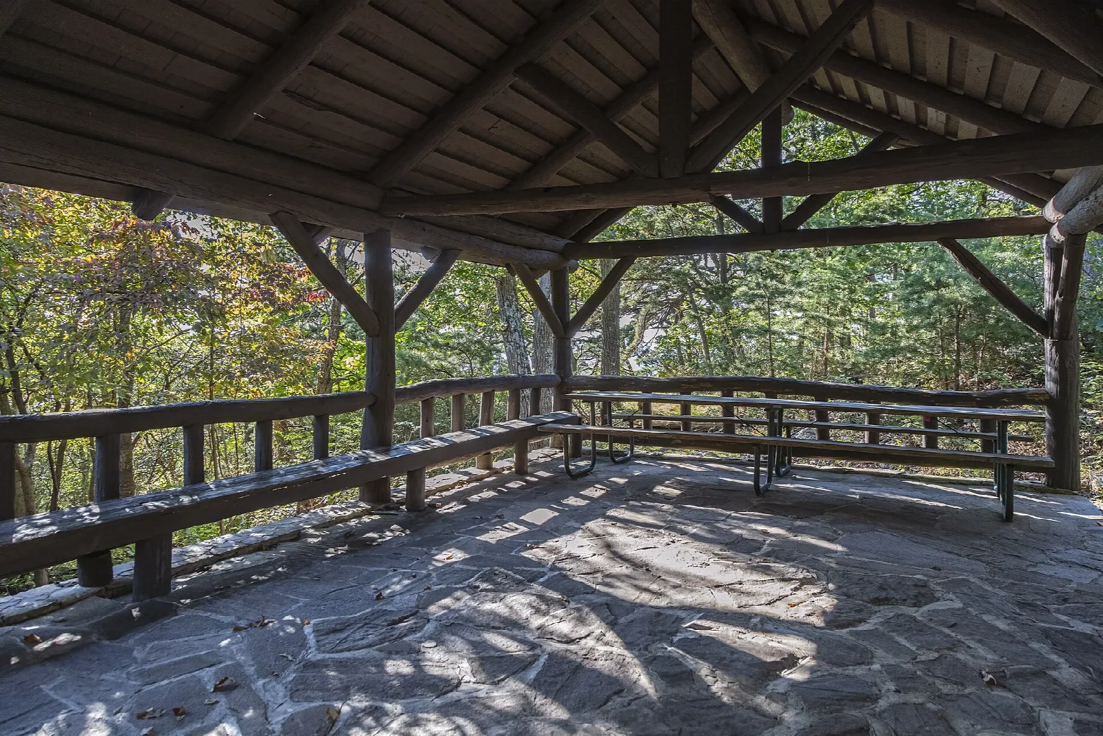 Open stone-floored wooden picnic shelter with benches and wooded views