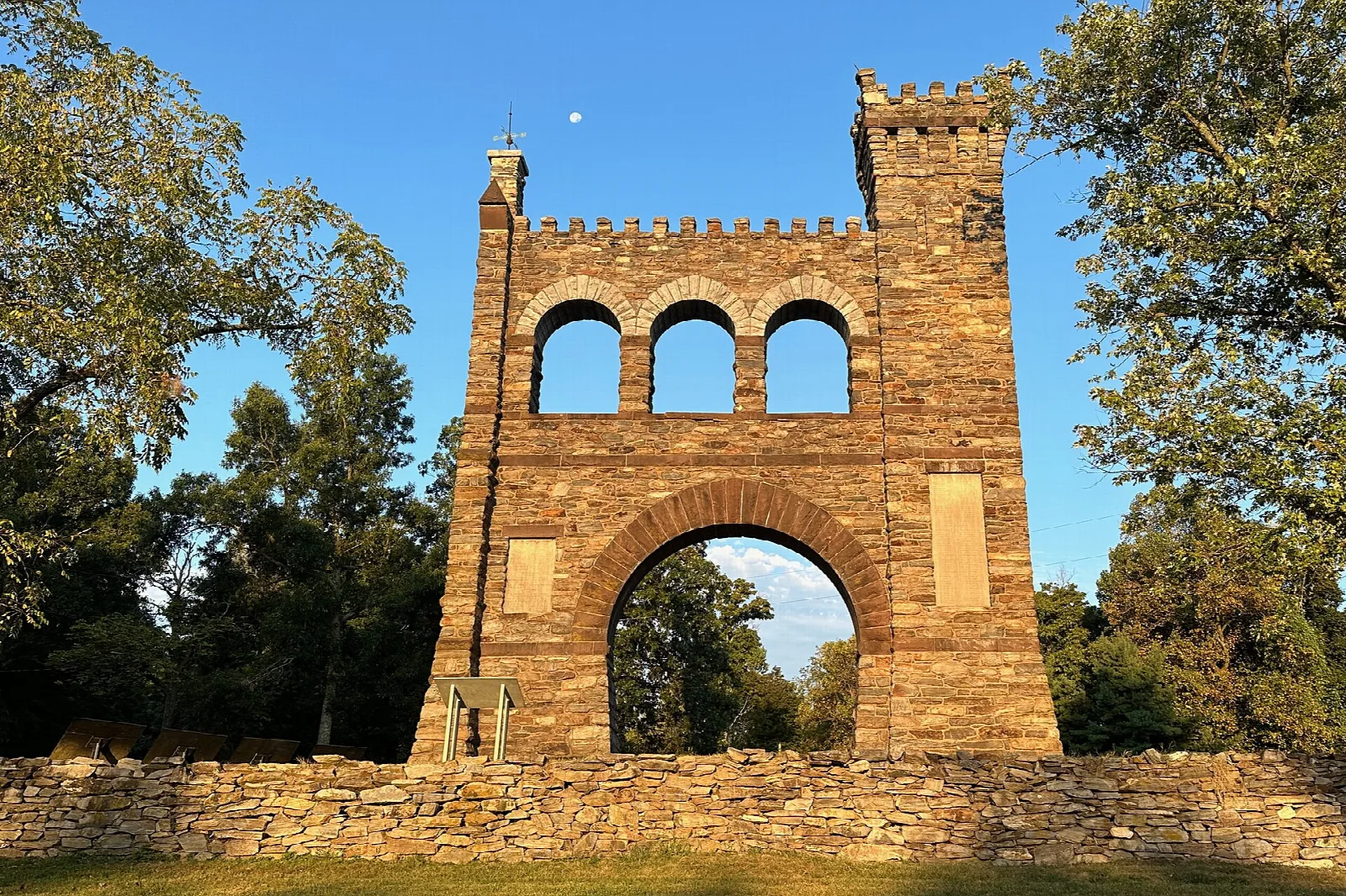 Stone memorial arch glowing in warm light among green trees