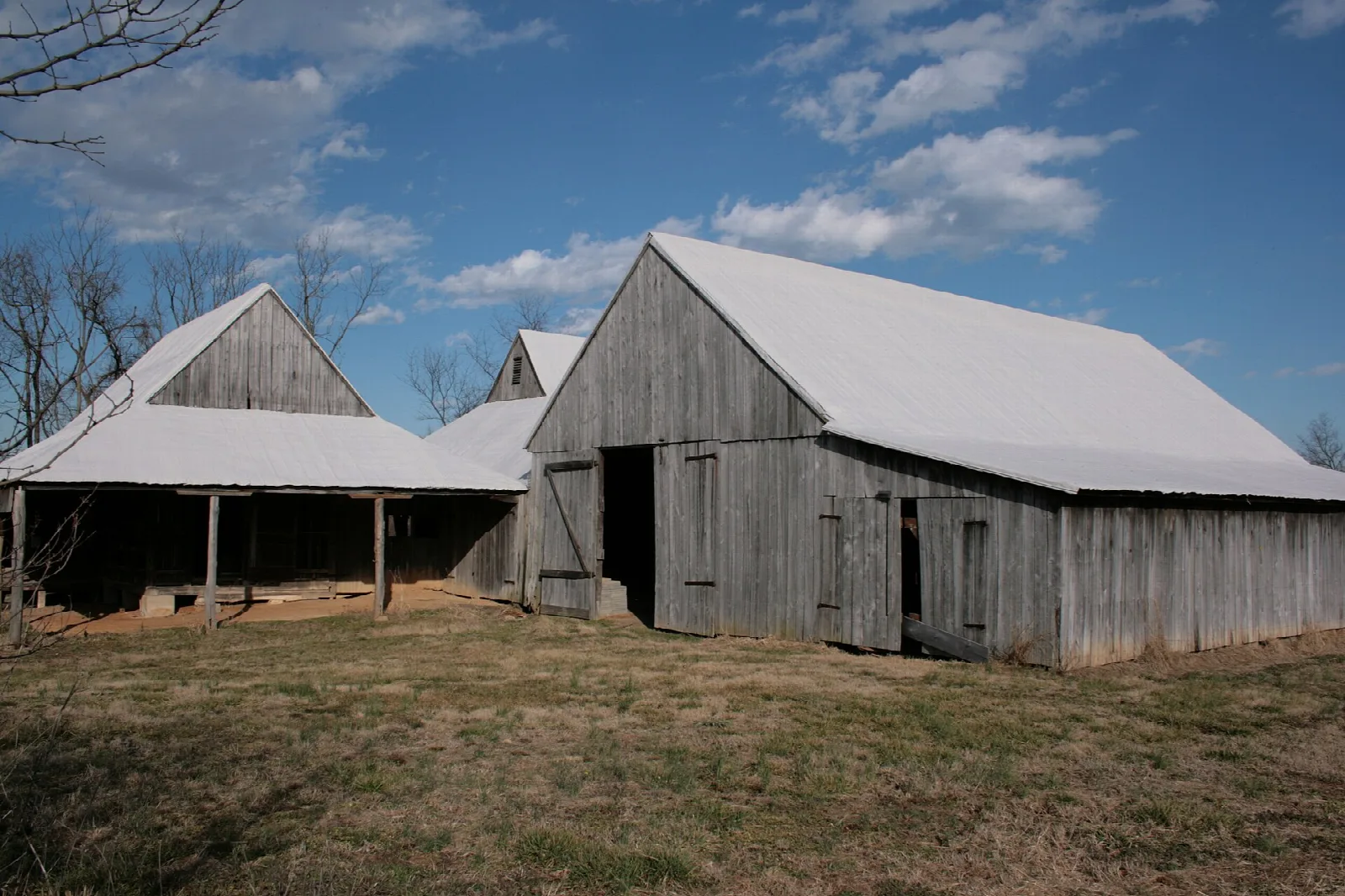 Weathered gray barns with white metal roofs under a blue sky