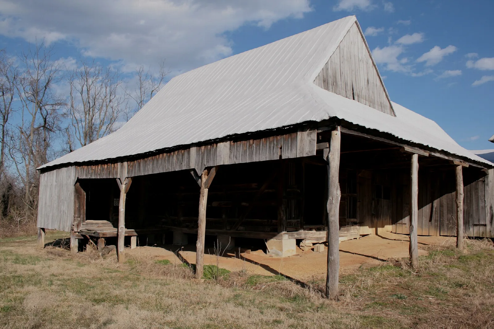 Open-sided gray barn with a white metal roof on dry grass