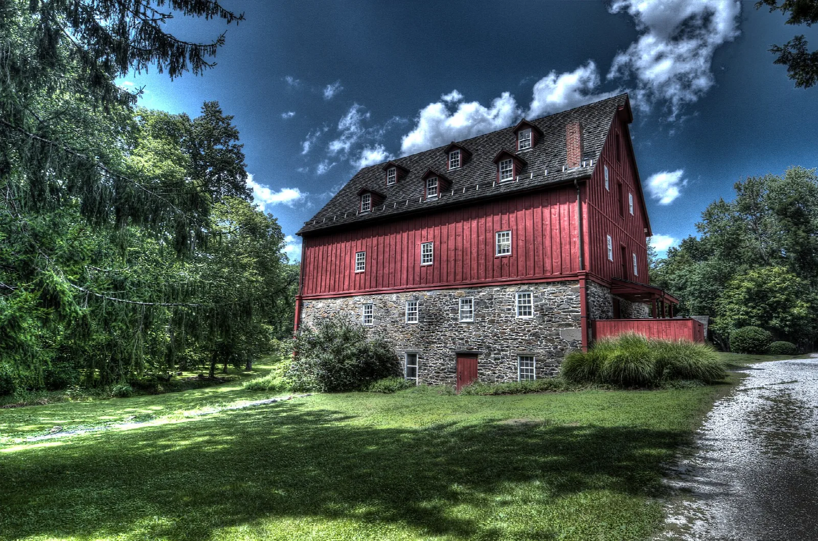 Red mill building with stone foundation above a wet gravel path and lawn