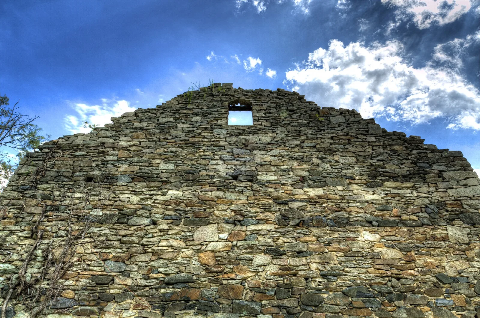 Stone gable wall with a small window against a blue sky