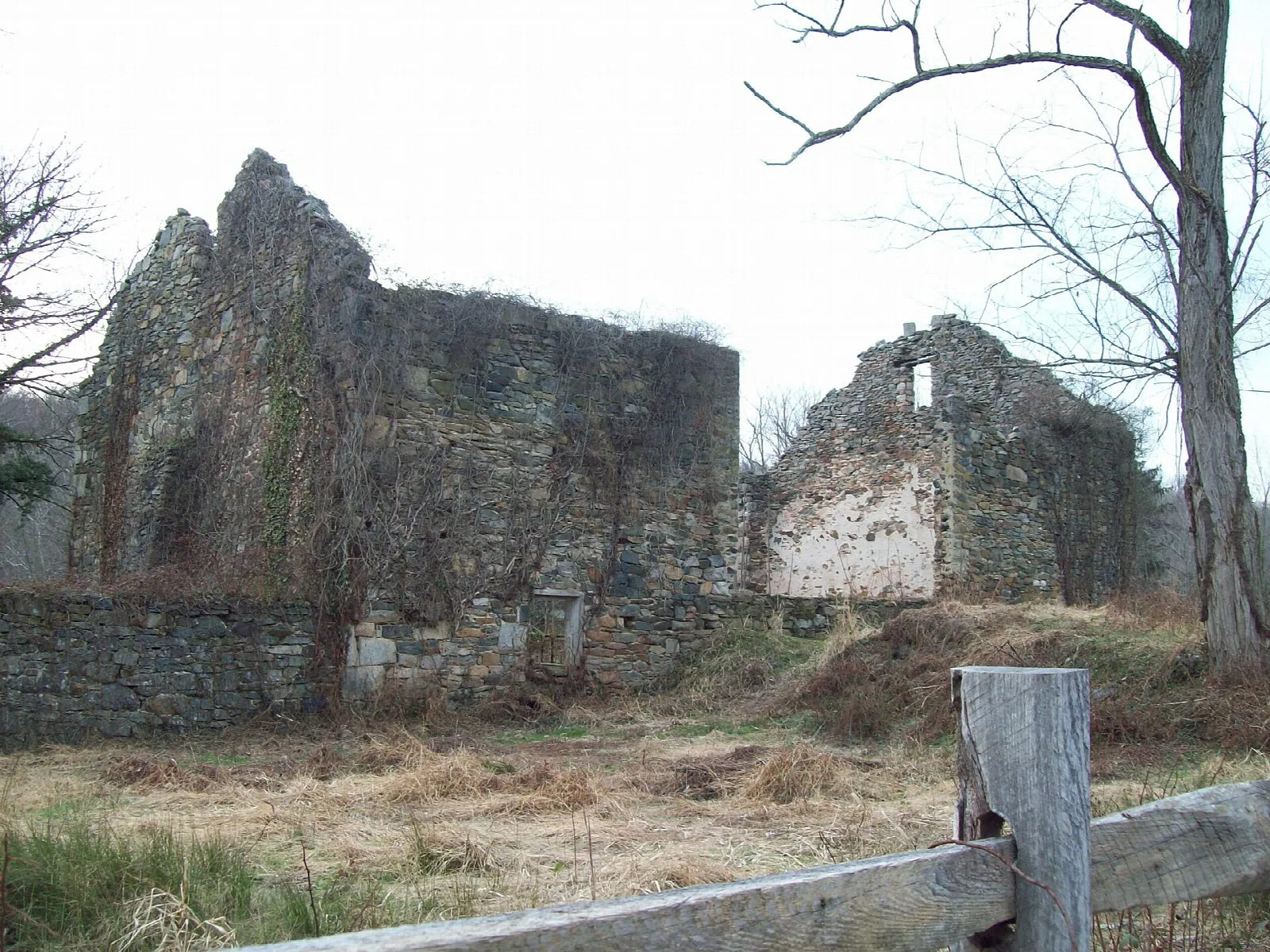 Weathered stone ruins of a barn behind a split-rail fence