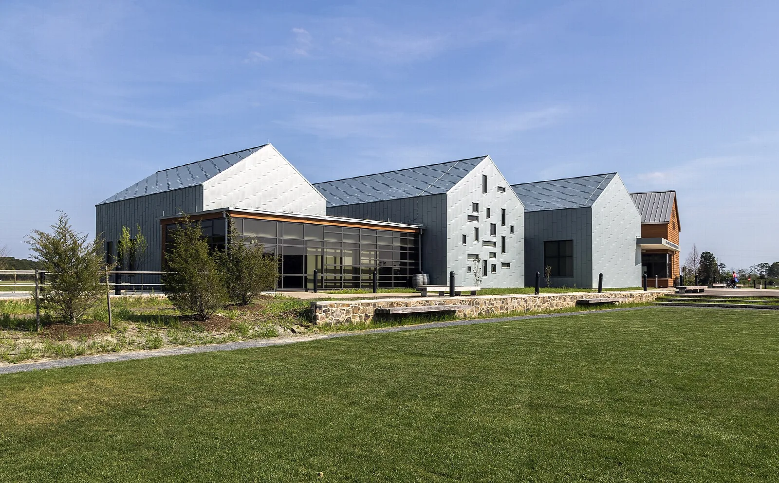 Modern gray gabled visitor center building beside a mown lawn under blue sky