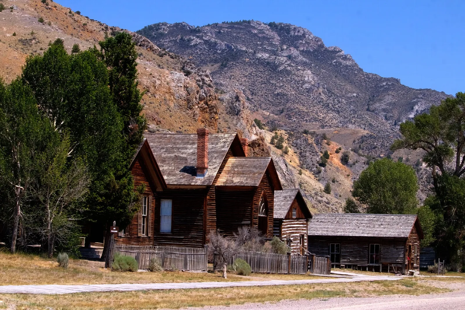 Weathered log house with a steep roof below a rocky mountain