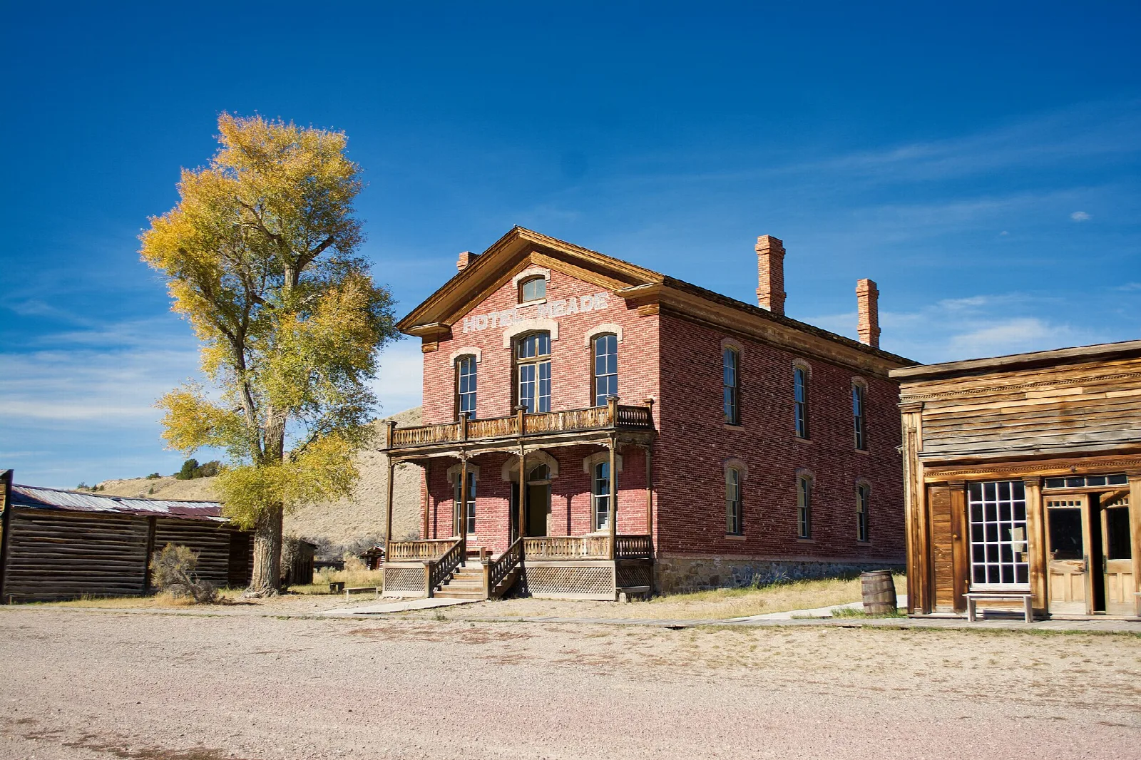Red brick two-story hotel with a balcony beside a yellow-leafed tree