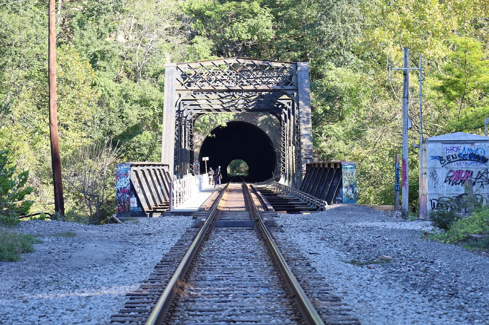 Railroad track leading into a stone tunnel beside an iron bridge