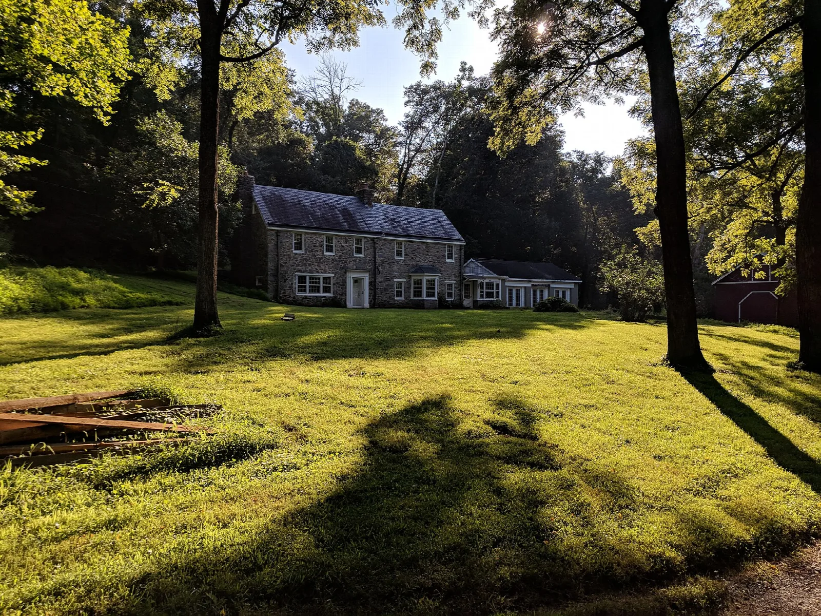 Stone farmhouse set back on a sunlit lawn among tall trees