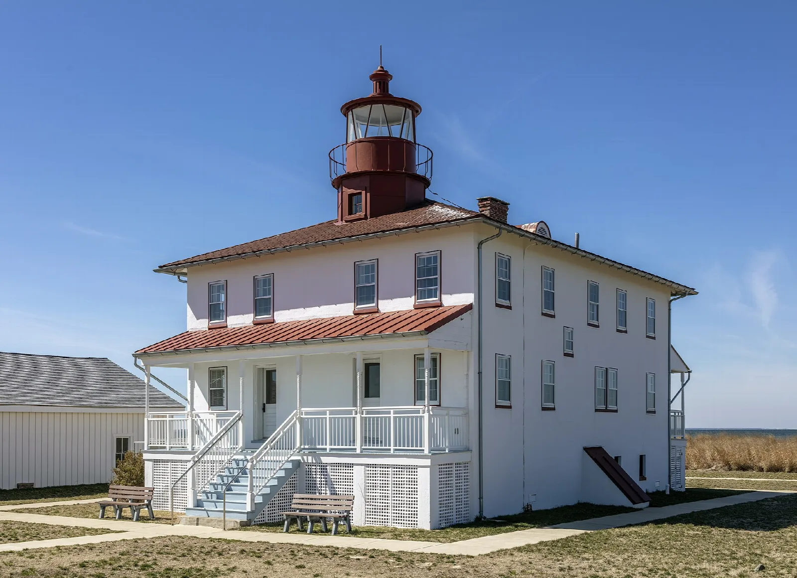 White two-story lighthouse building with a red roof under blue sky
