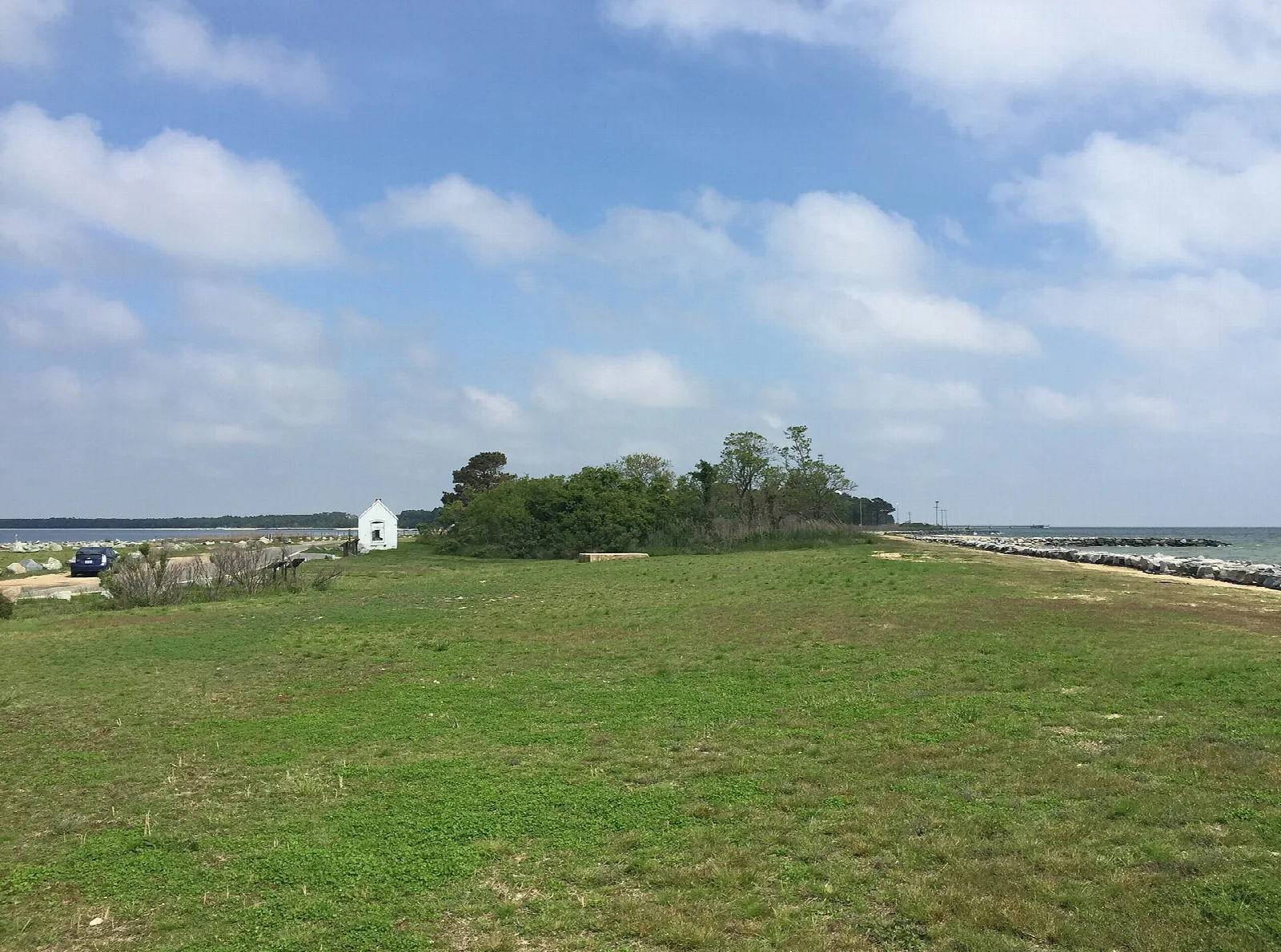 Green field with trees and a small white building near the water