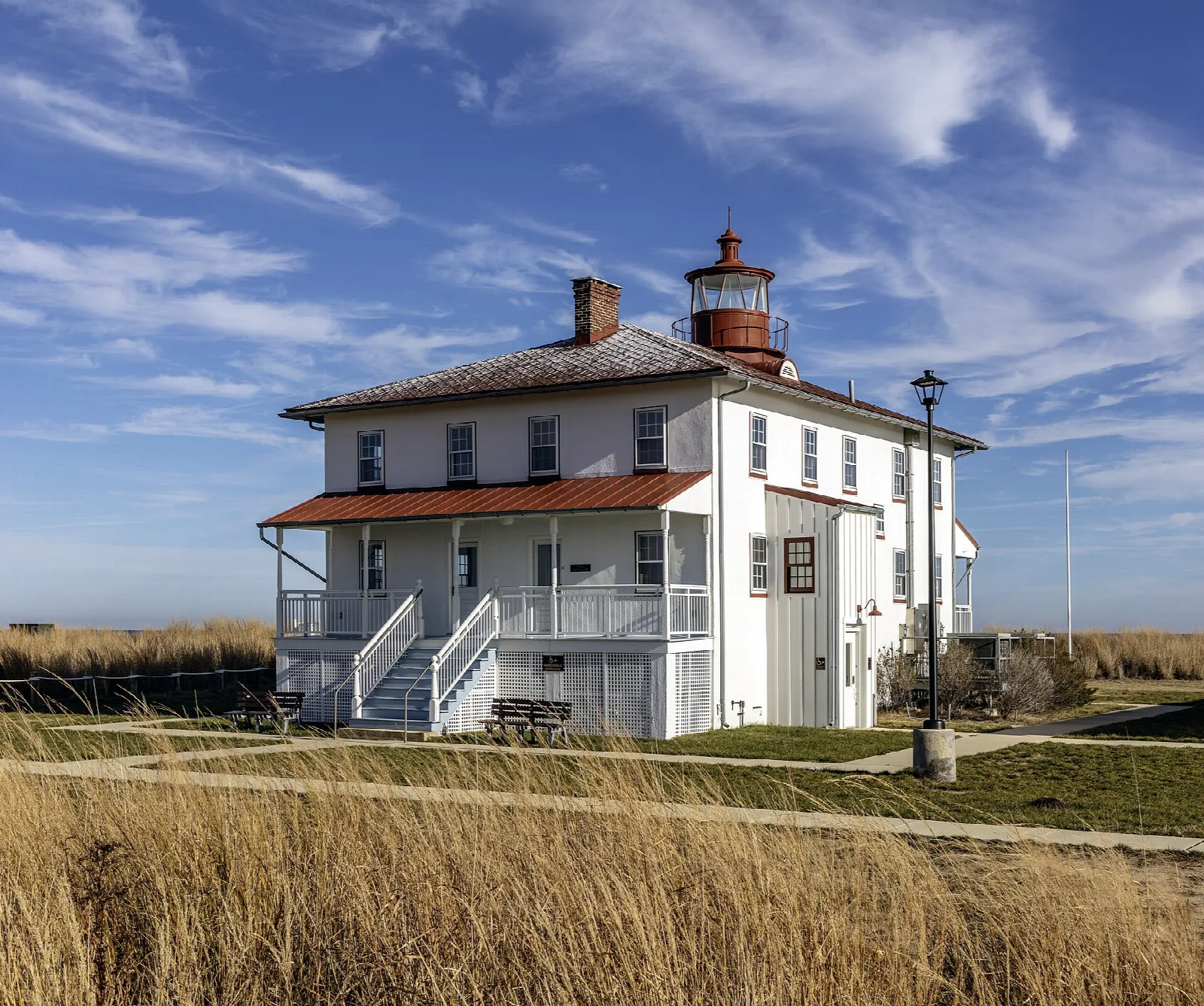 White lighthouse building with a lantern tower above golden grass