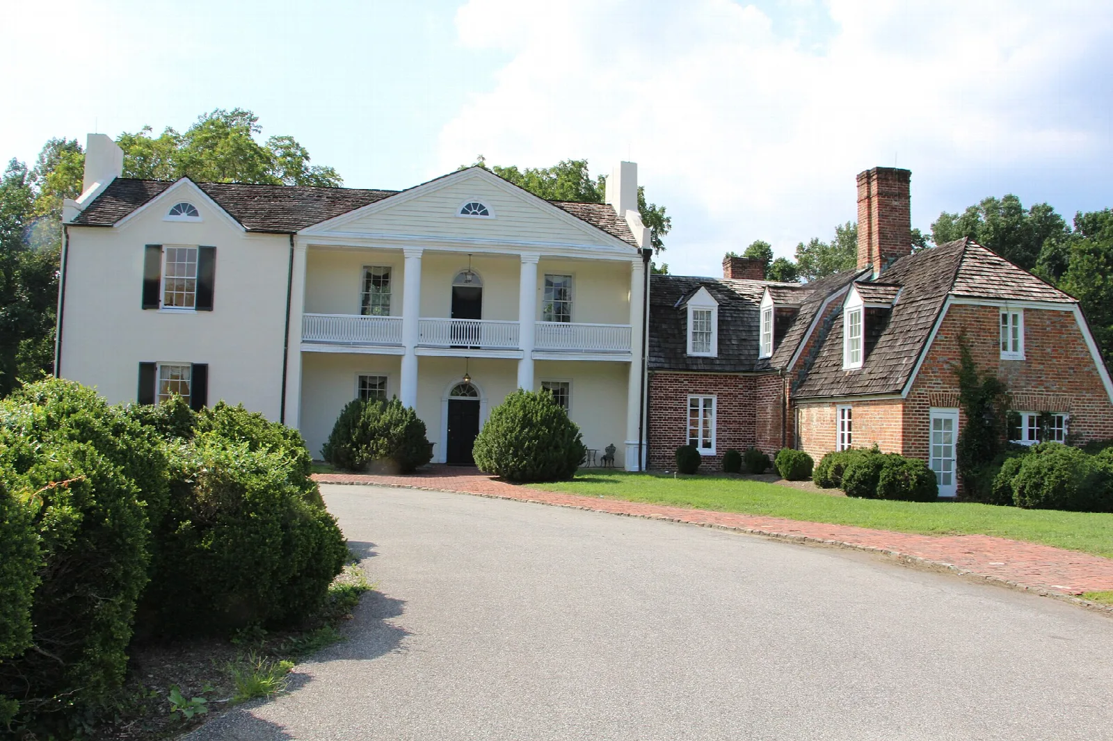 White manor house with a two-level porch behind trimmed shrubs