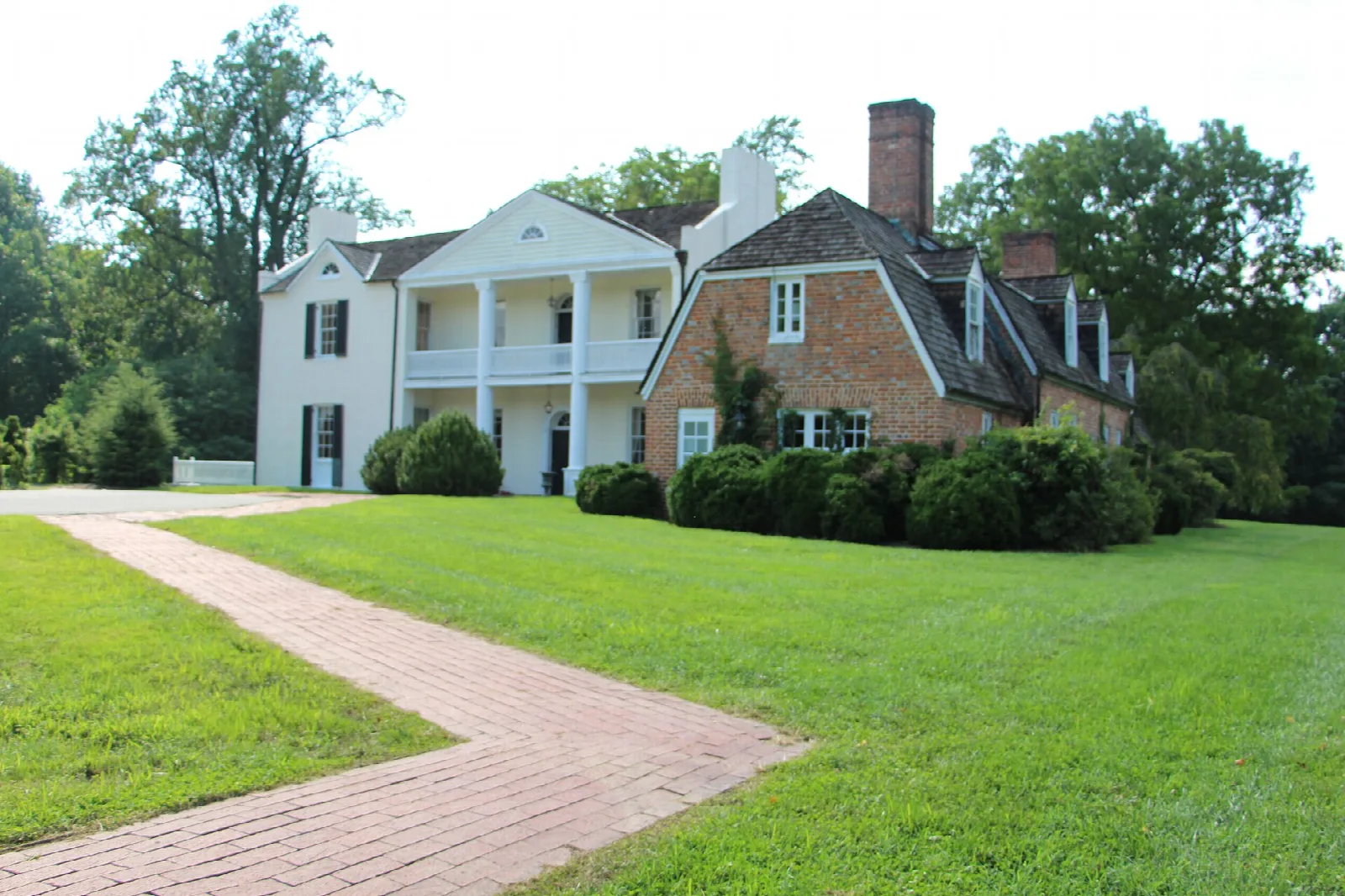 White manor house with a columned porch behind a brick path and lawn