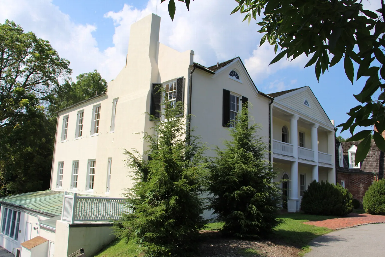 Side view of a pale manor house with chimneys and evergreen shrubs