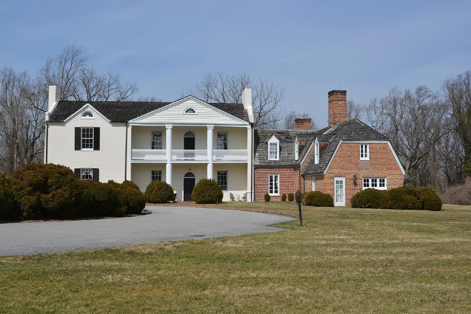 White two-story manor house with a columned porch and brick wing across a lawn