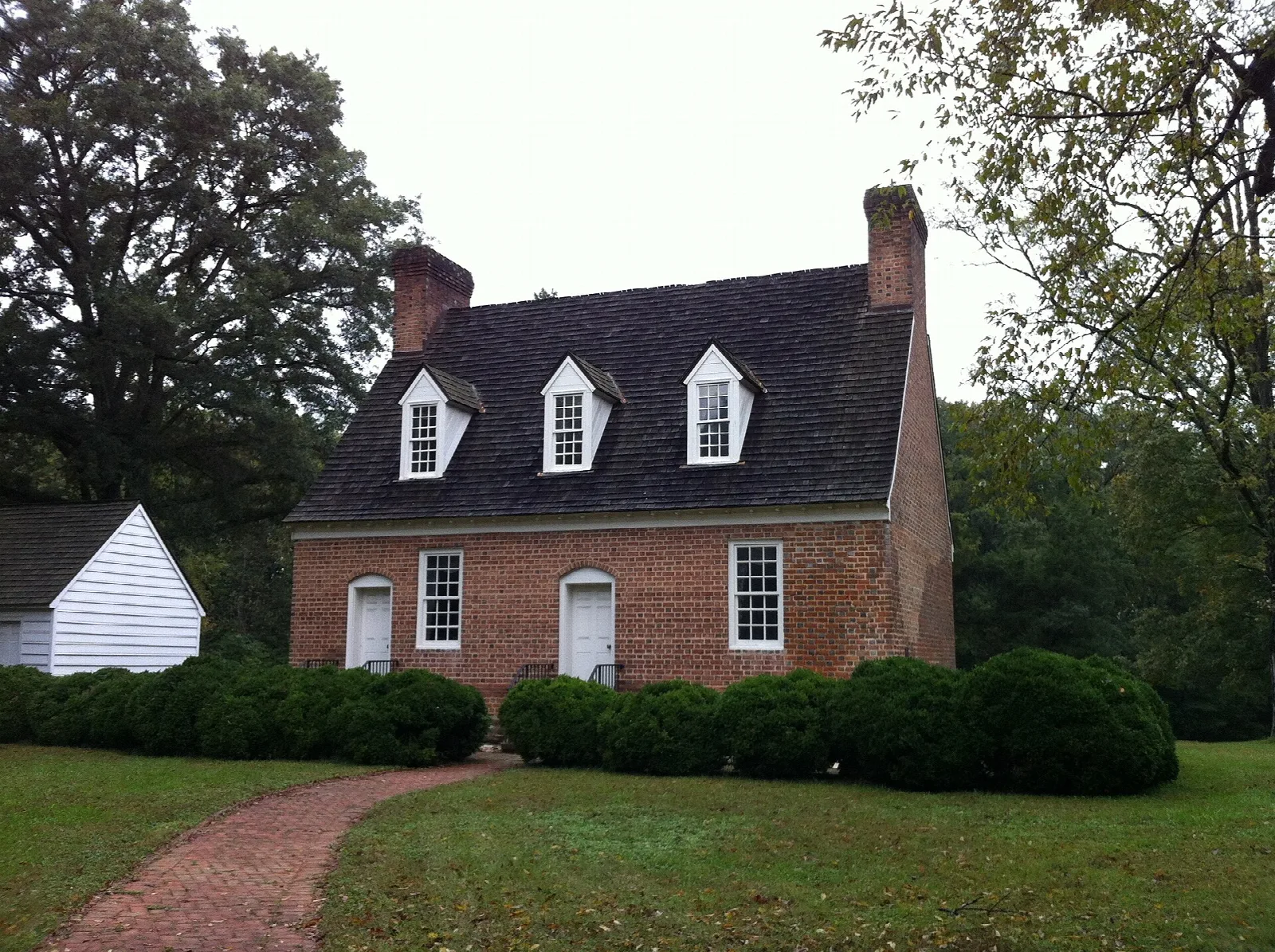 Brick house with a dark roof and white outbuilding beside a brick path
