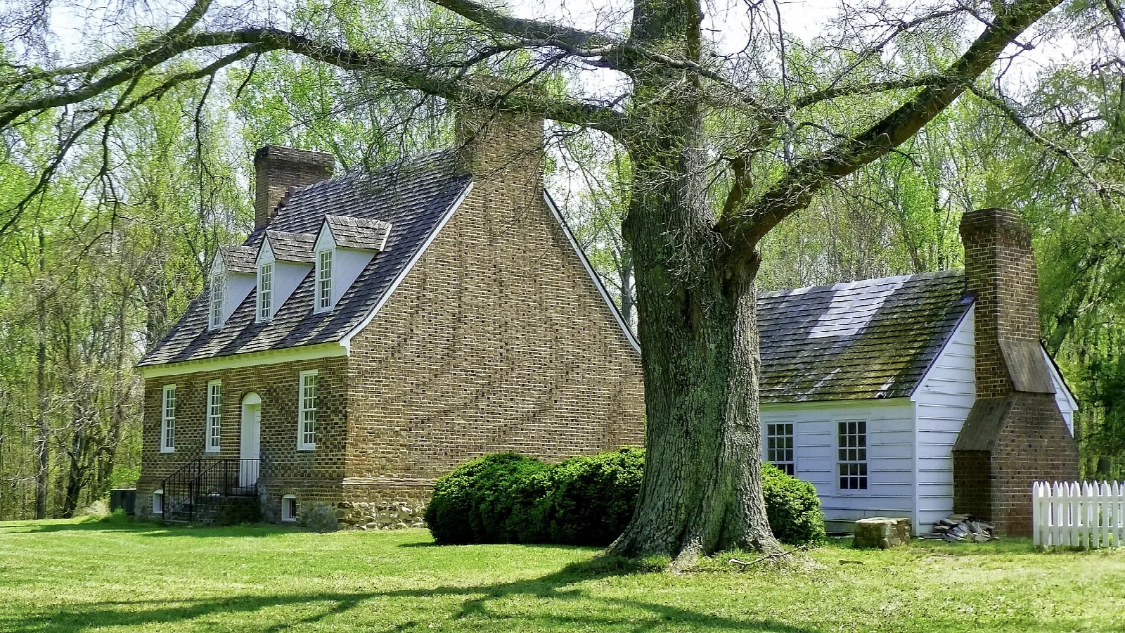 Old brick and stone house with dormer windows under a large tree