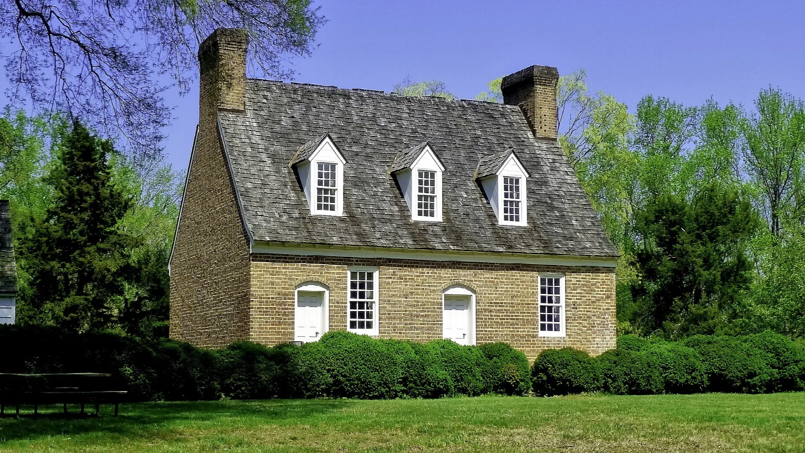 Stone house with dormers and a hedge on a sunny lawn
