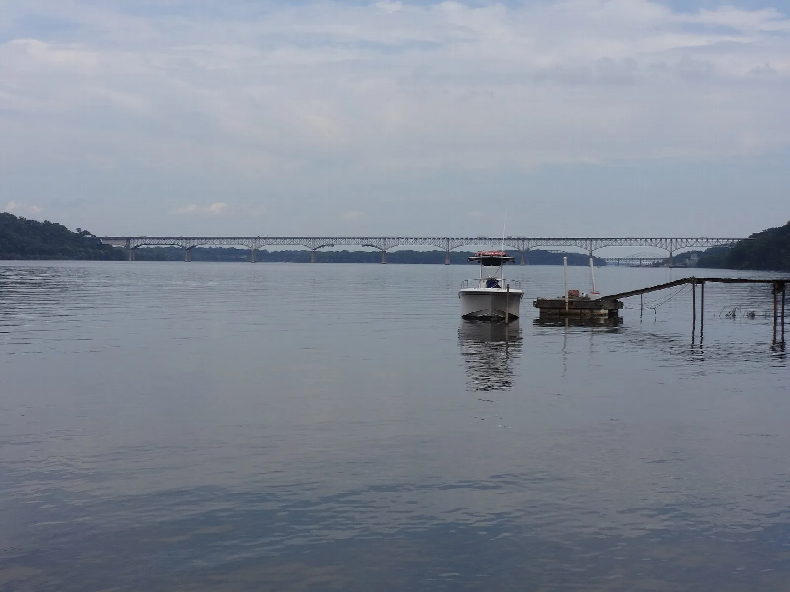 Boat tied near a pier on the river with a long bridge behind