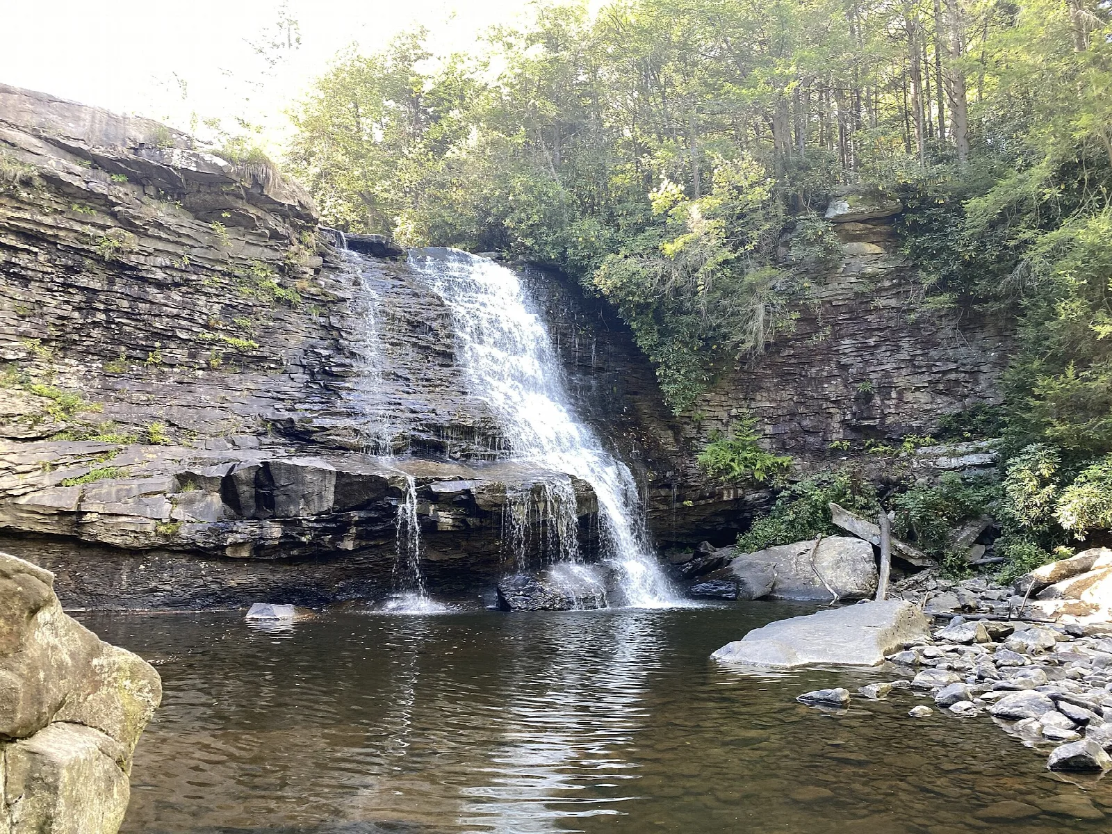 Waterfall over a layered rock wall into a pool under trees