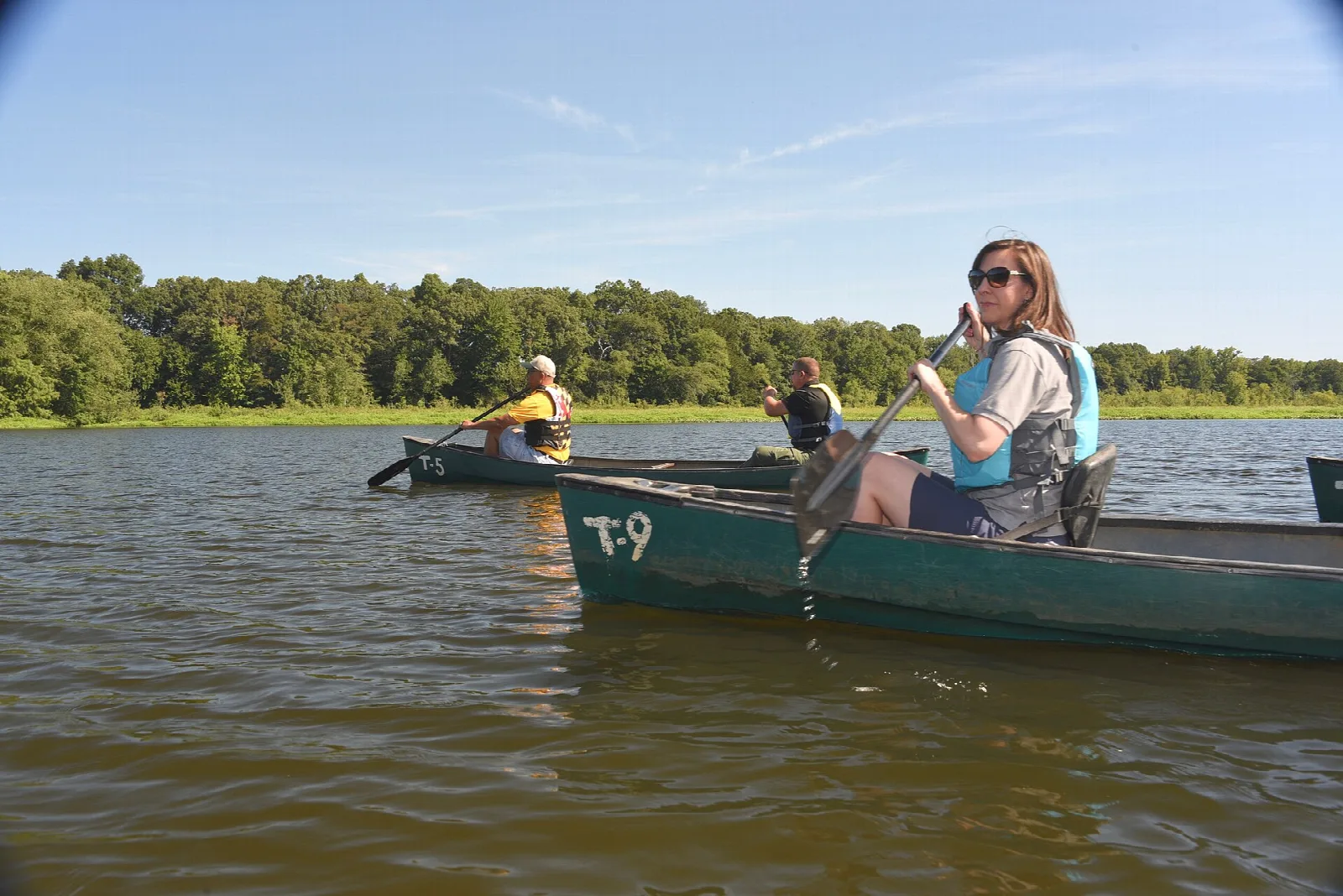 Two canoes with paddlers on a calm lake with trees along the shore
