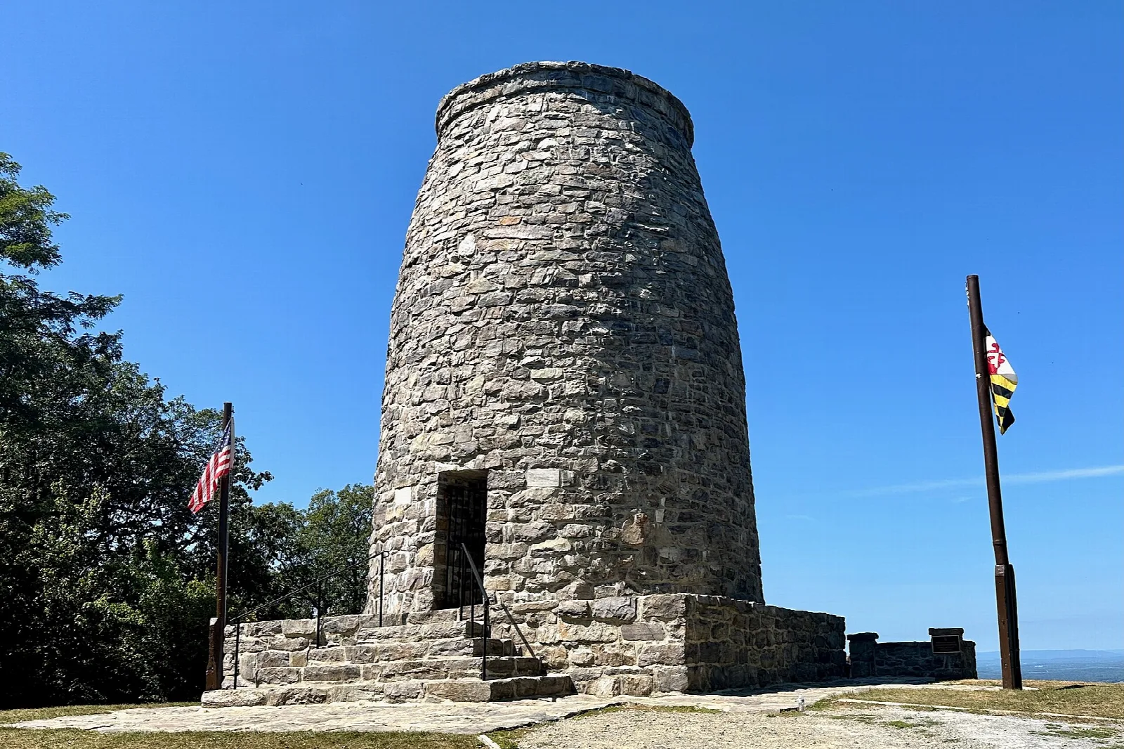 Round stone tower on a hilltop with a Maryland flag under blue sky