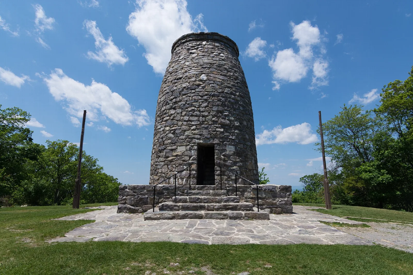 Stone tower on a paved platform with trees and clouds behind