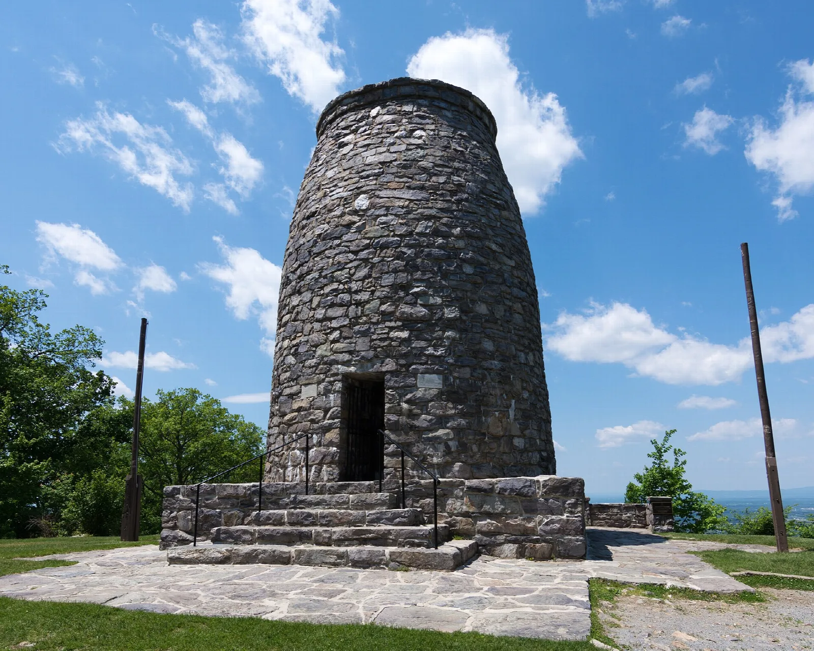 Stone tower seen from a low angle on a paved pad under blue sky