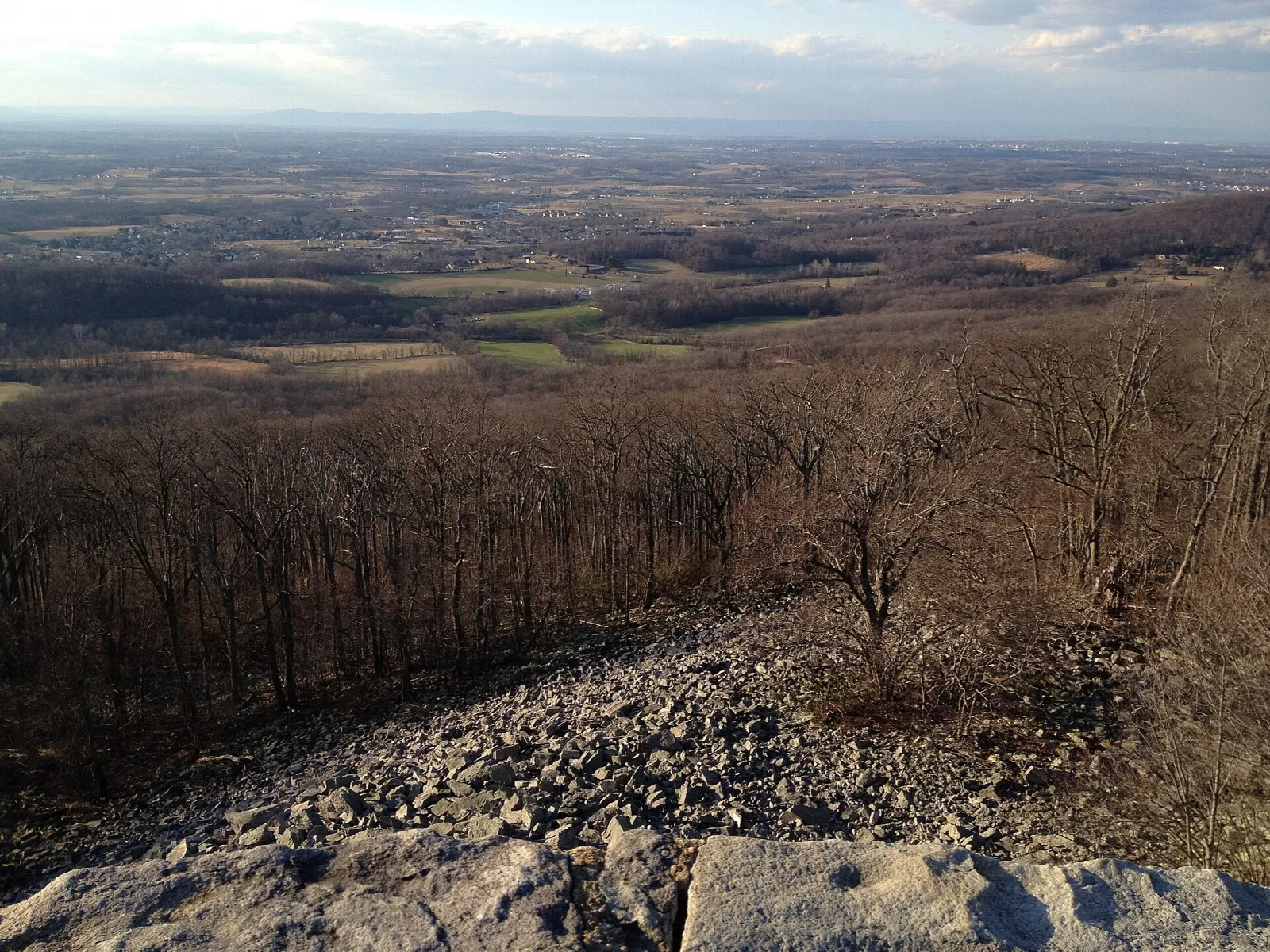 View over farmland and ridges from a rocky hilltop with bare trees