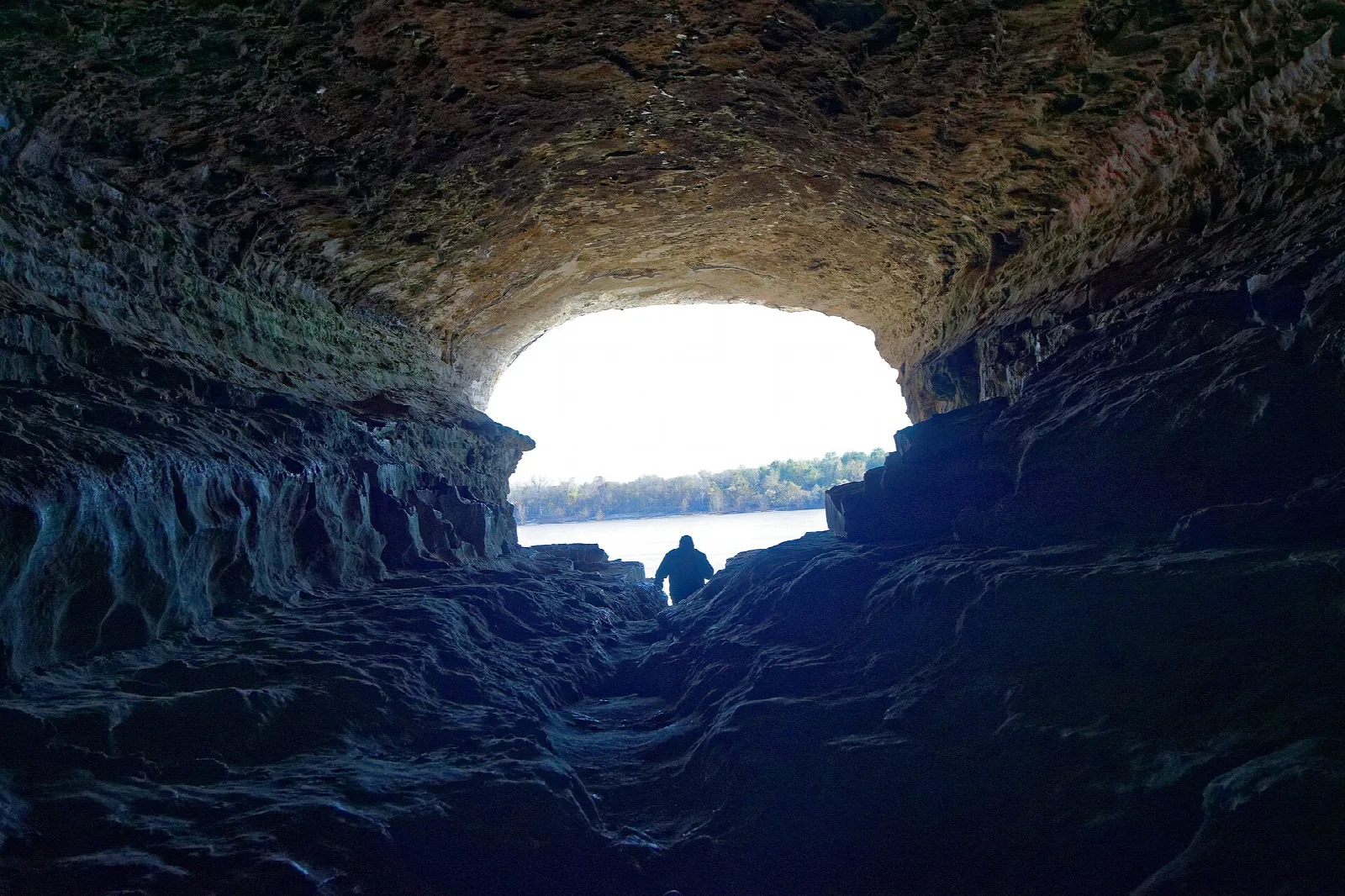 Silhouette of a person at a bright cave opening above the river