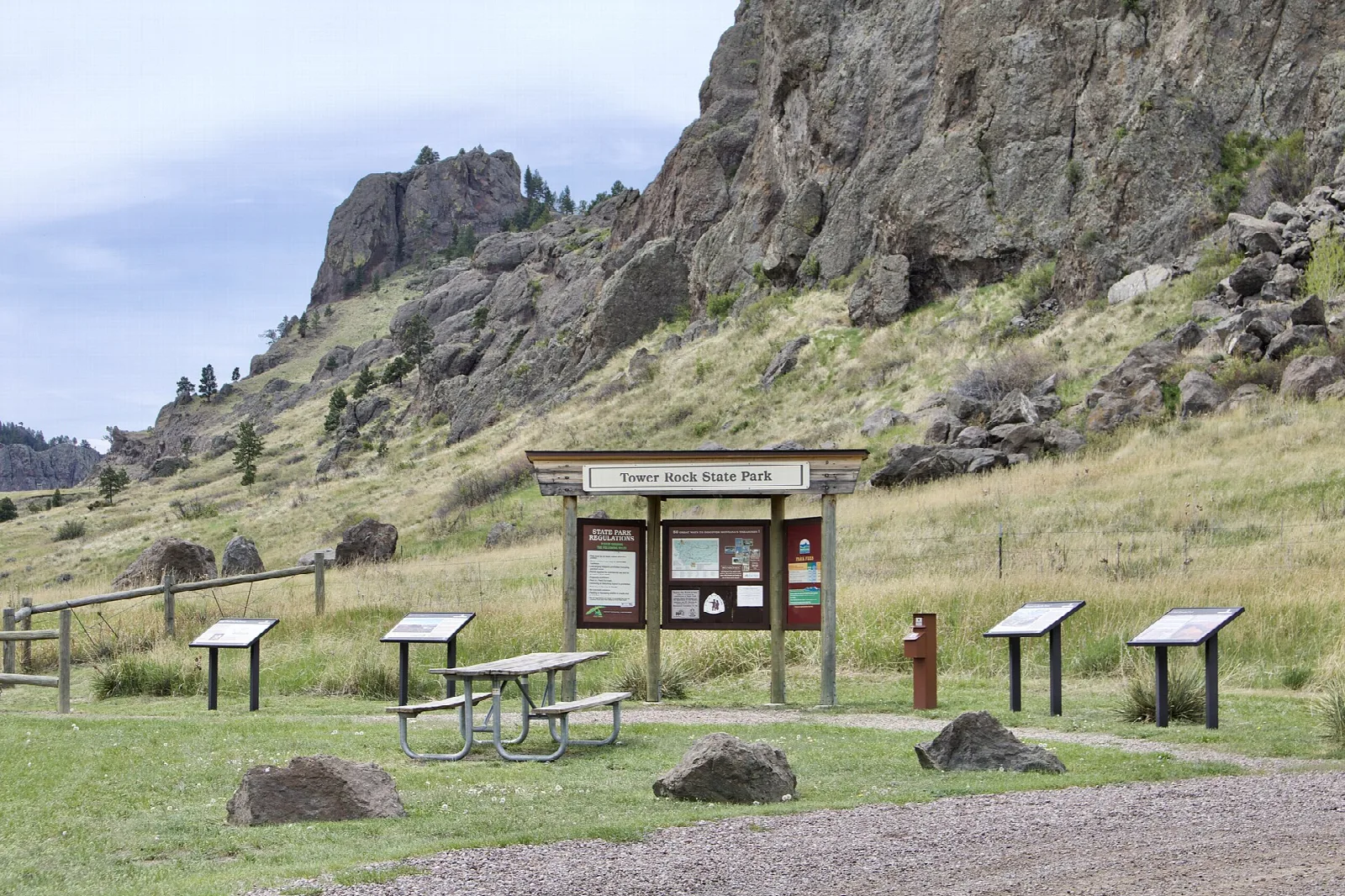 Rocky formation above a grassy slope with a picnic table and signs