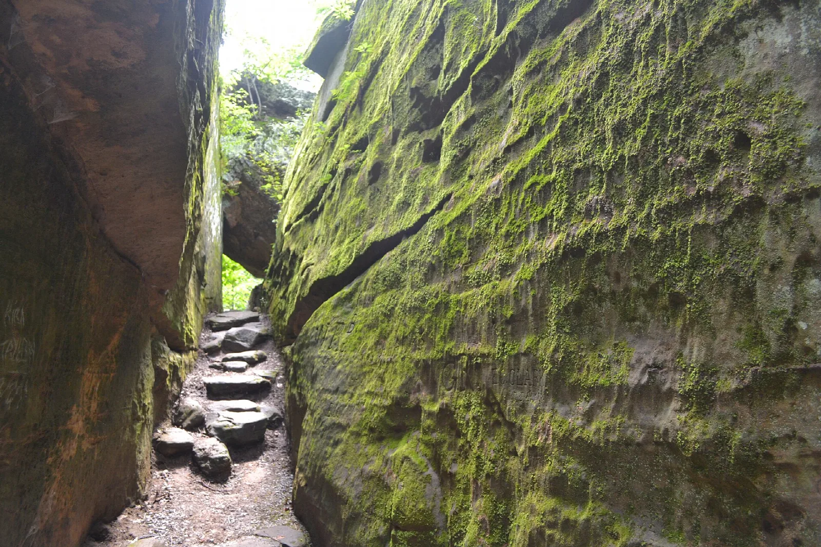Narrow passage between two tall moss-covered sandstone blocks with steps