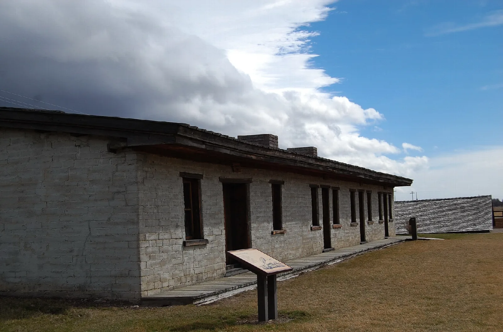 Long low adobe barracks with an interpretive sign in front