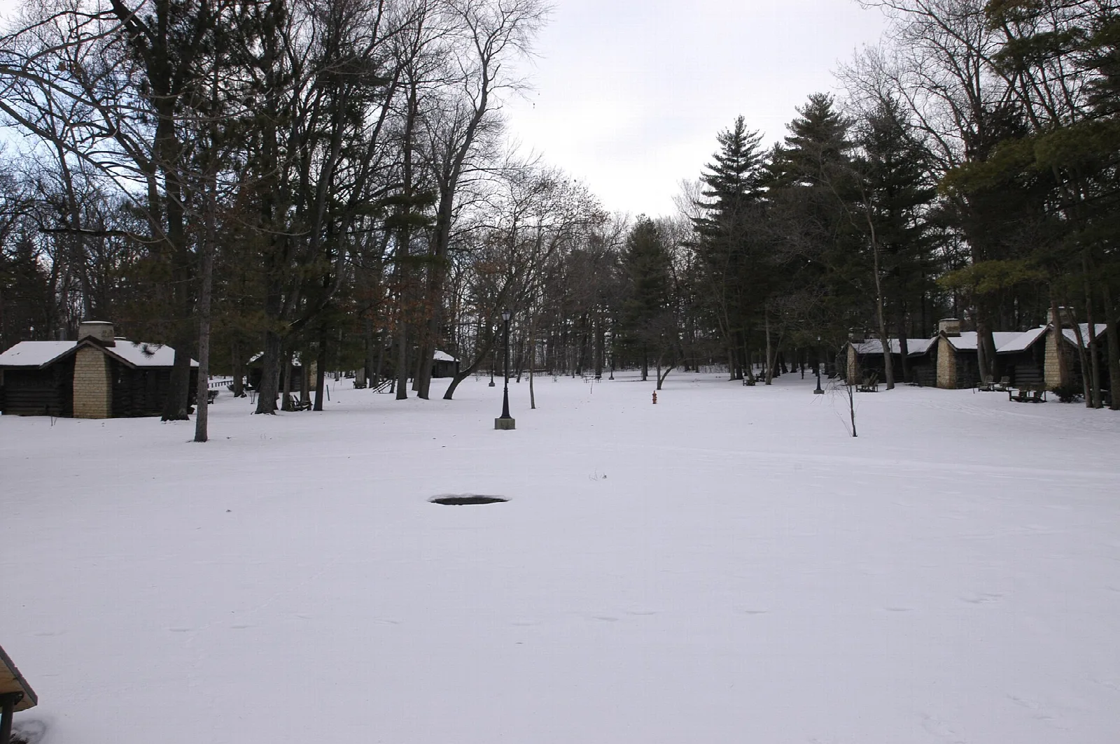Snowy clearing with log cabins among trees