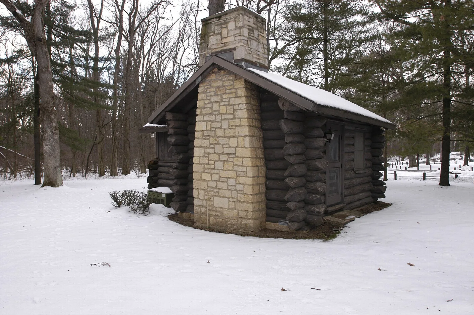 Log cabin with a stone chimney in snow among trees
