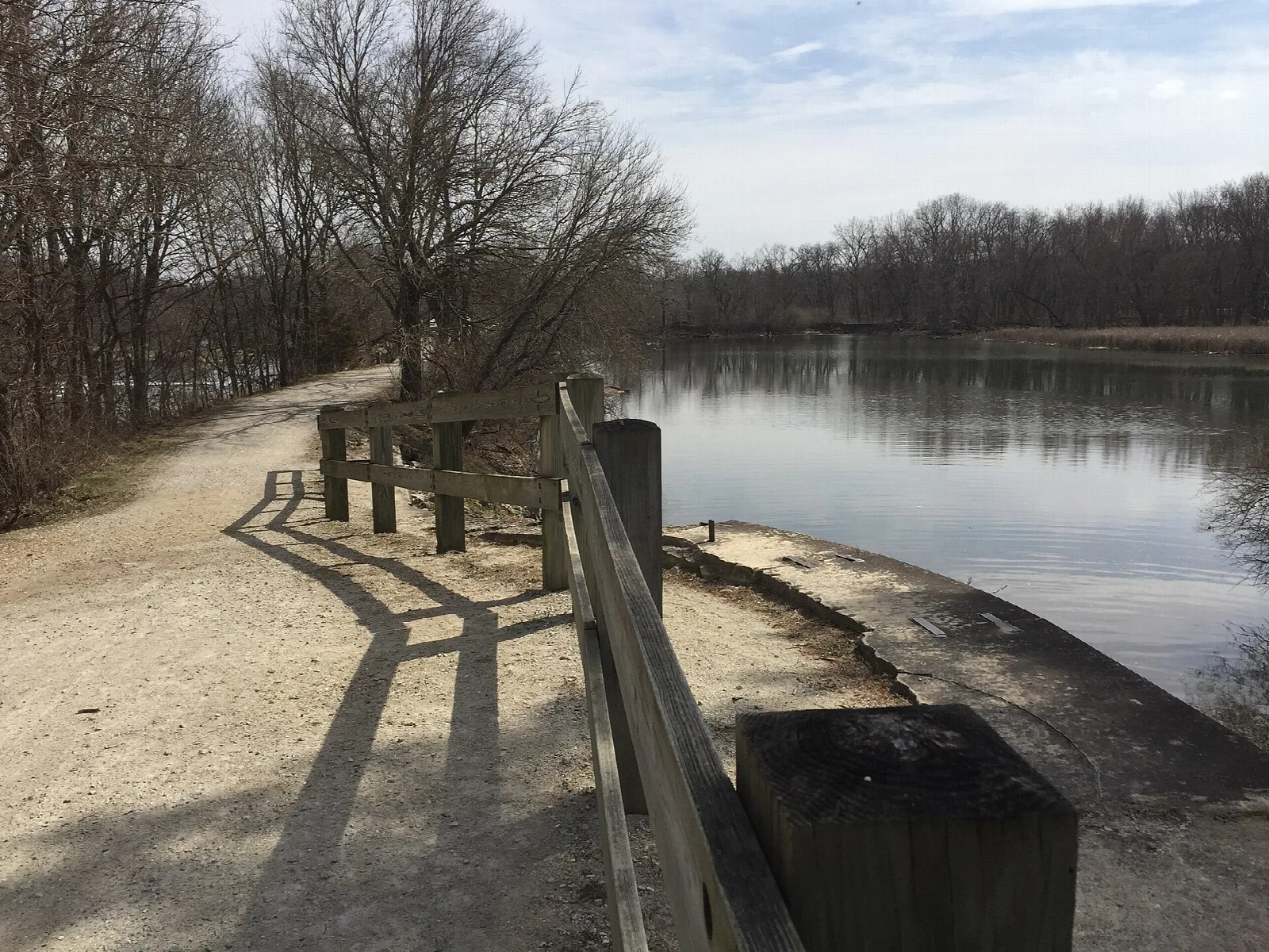 Gravel path and wooden railing beside calm water